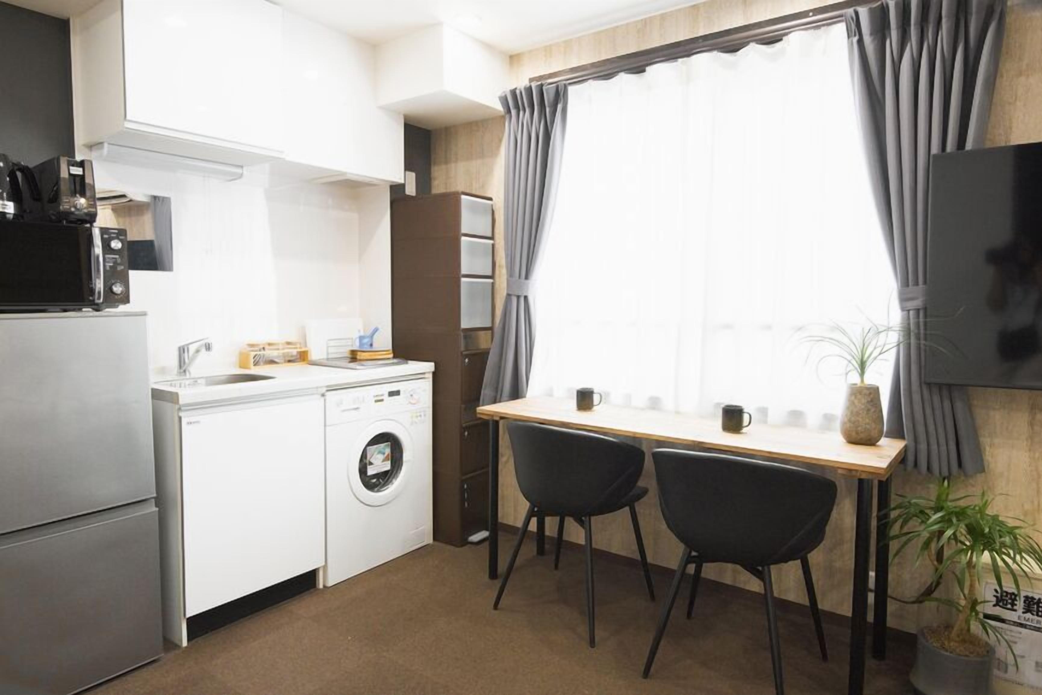 Cocina compacta con lavadora, microondas y un pequeño comedor con dos sillas.