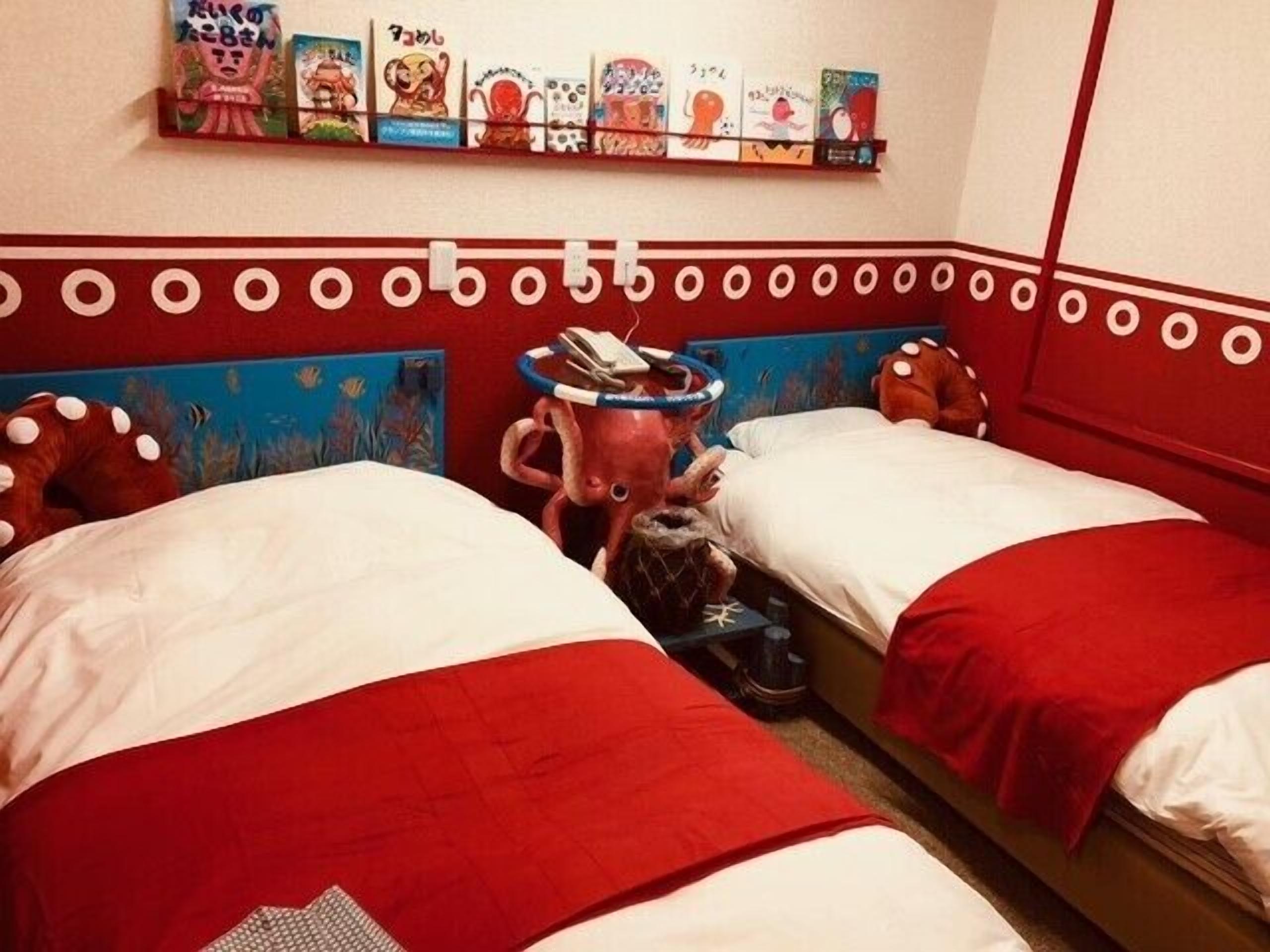 Habitación de hotel con dos camas, un estante con obras de arte de colores y una original cabecera con temática de pulpo.