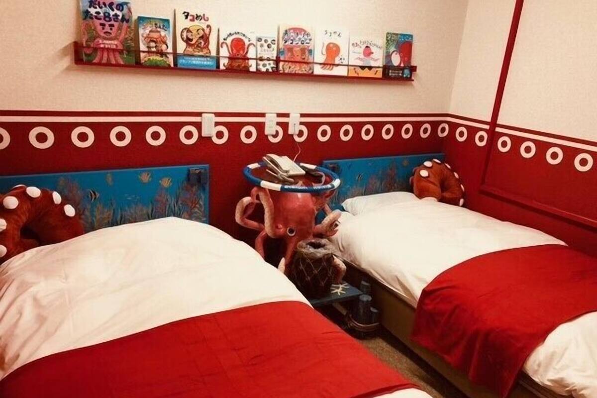 Habitación de hotel con dos camas, un estante con obras de arte de colores y una original cabecera con temática de pulpo.