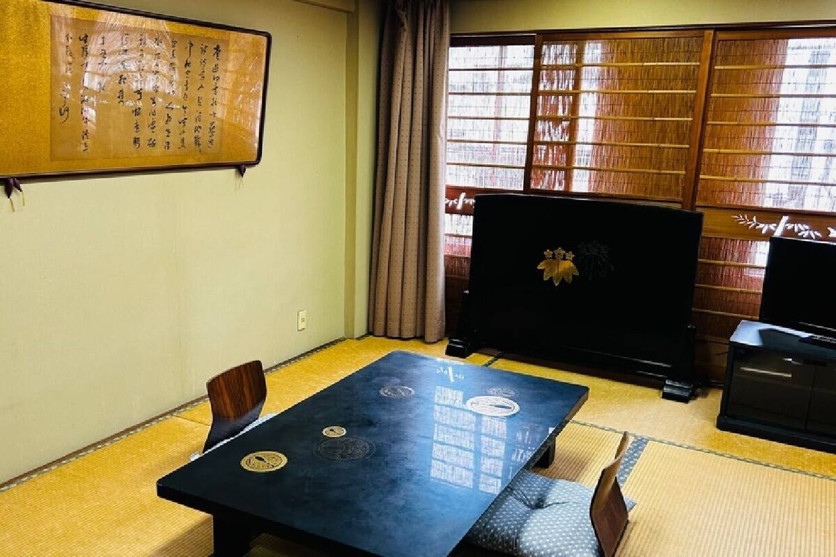 Una habitación con suelo de tatami, una mesa baja con cojines, un televisor y una obra de caligrafía japonesa tradicional en la pared.