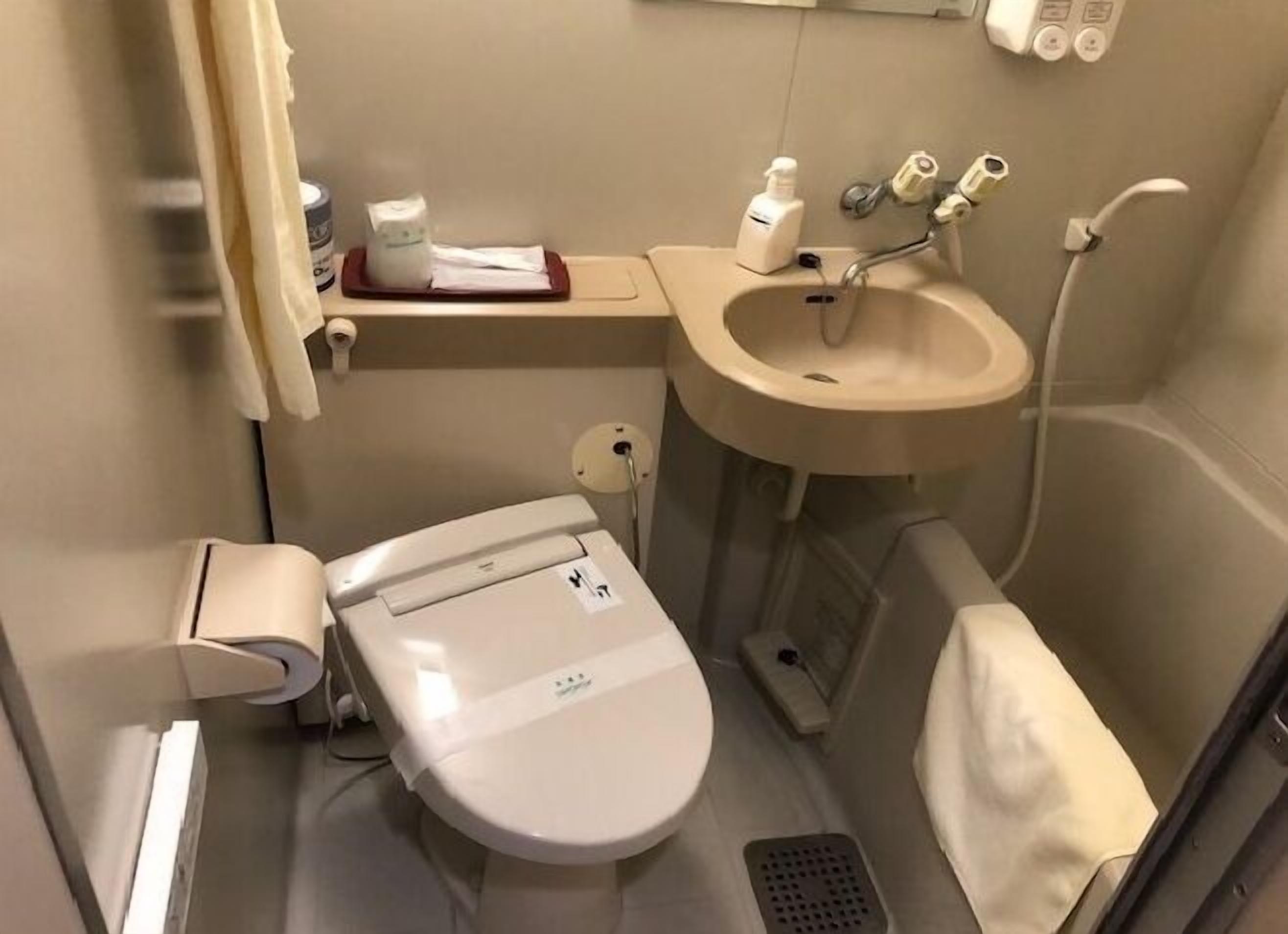 Un baño pequeño con inodoro, lavamanos y un estante con artículos de aseo.