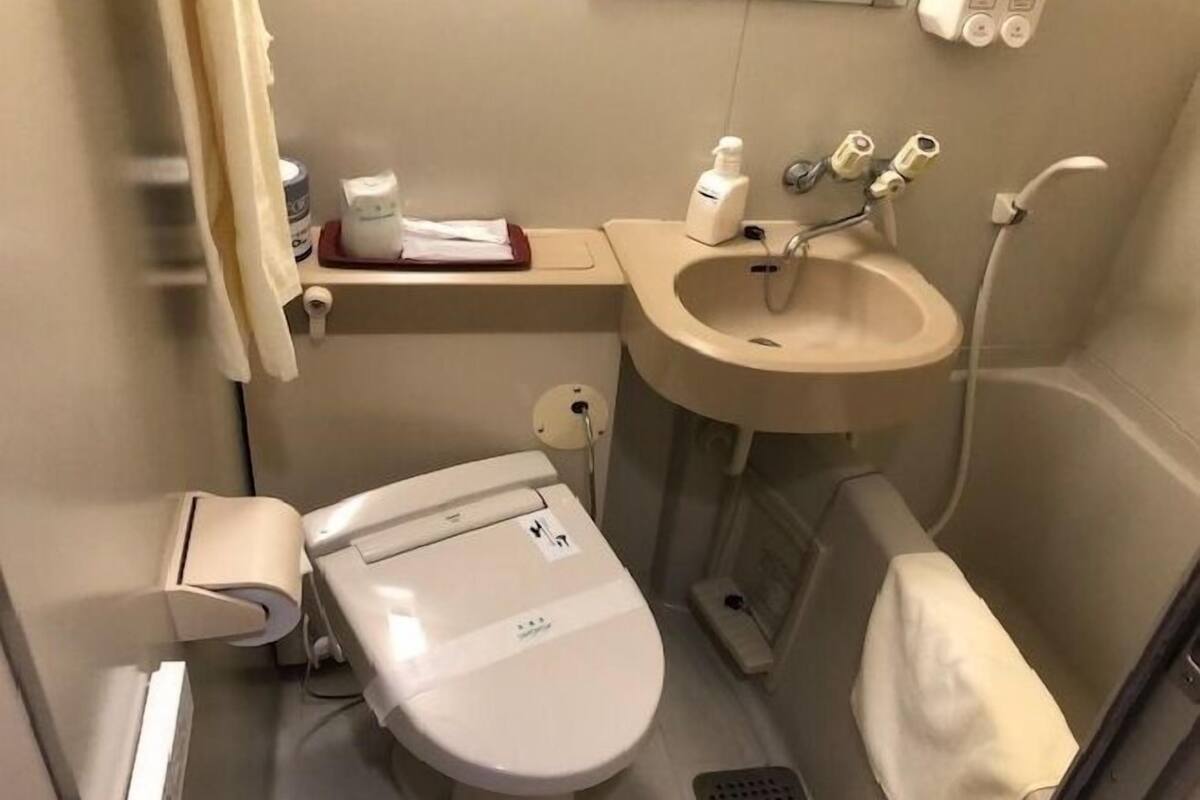 Un baño pequeño con inodoro, lavamanos y un estante con artículos de aseo.