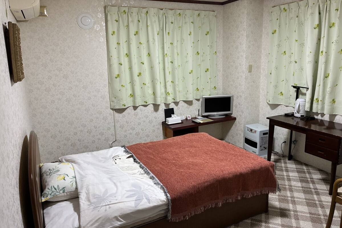 Un dormitorio con una cama, un escritorio, una silla, un televisor y un calentador pequeño.