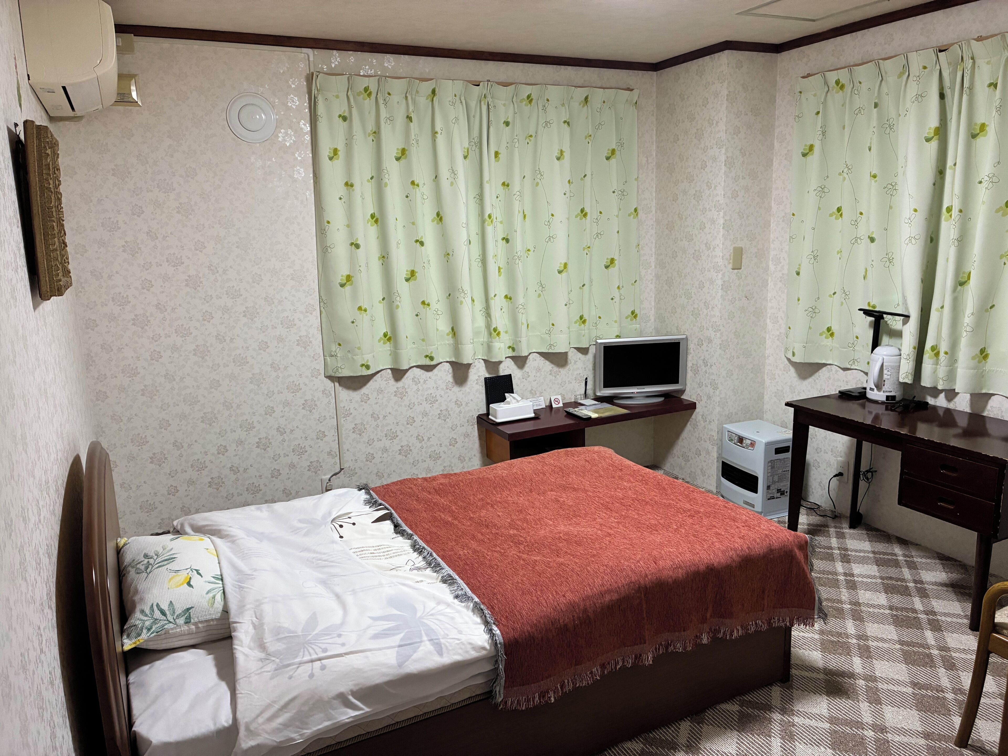 Ein Schlafzimmer mit einem Bett, einem Schreibtisch, einem Computer und einer Kaffeemaschine.