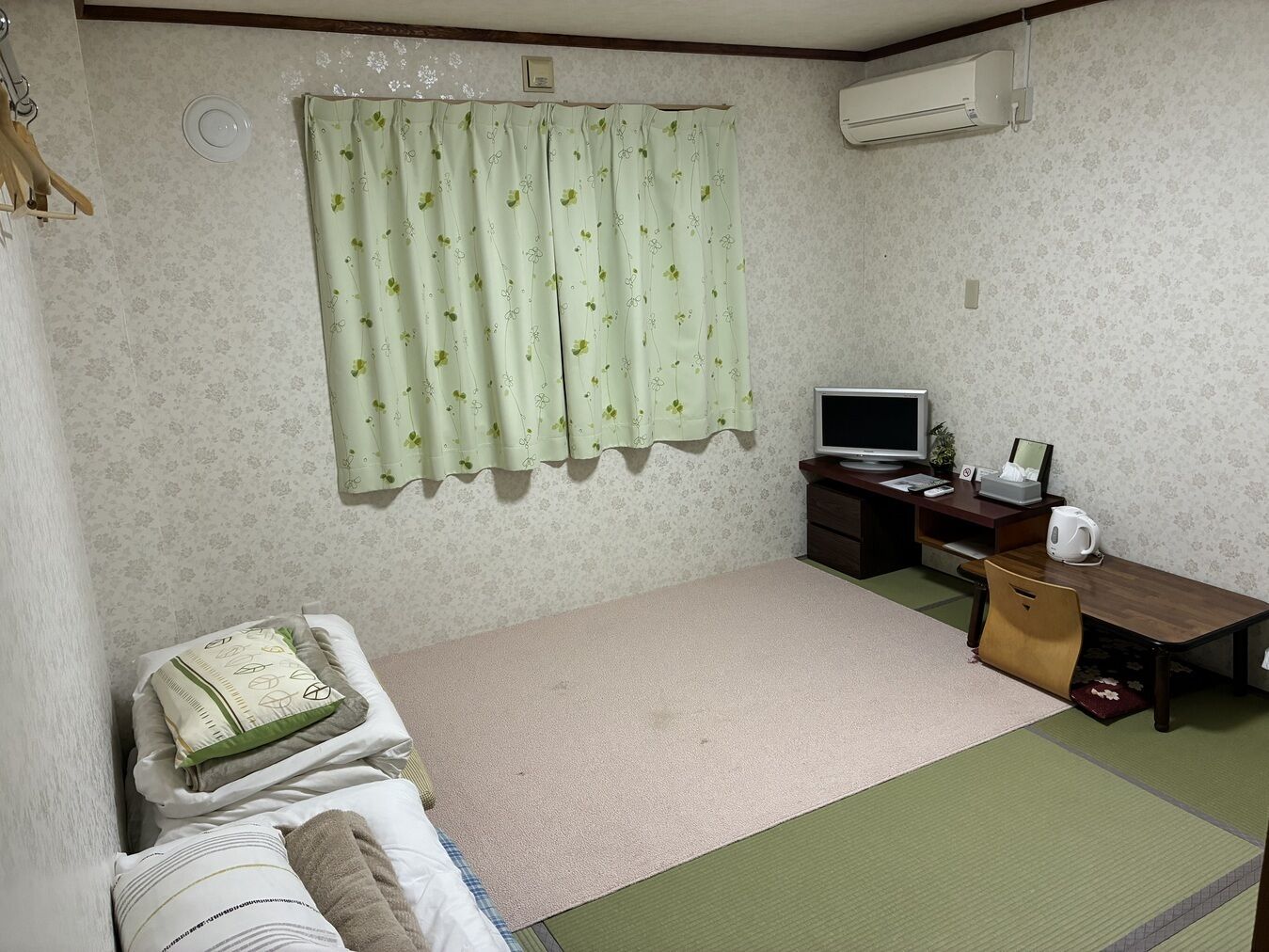 Quarto com uma cama, uma escrivaninha com computador, televisão e ar condicionado.