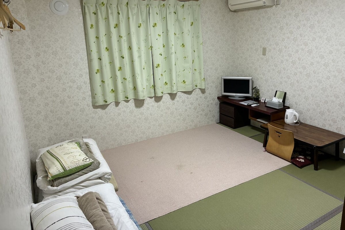 Una habitación con cama, escritorio con computadora, televisor y aire acondicionado.