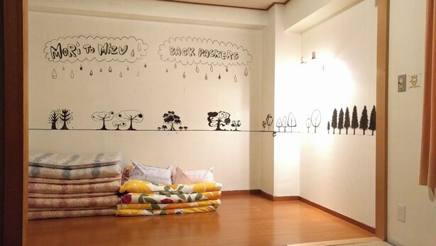 A room with a bed, pillows, a wall with drawings, and a wooden floor. - Moritomizu Backpackers (Nagano)