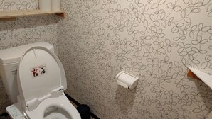A bathroom with a toilet, a toilet paper holder, and a shelf with toilet paper. - Moritomizu Backpackers (Nagano)