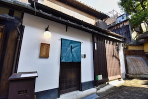 A traditional Japanese building with a wooden gate, a blue hanging cloth, and a white wall. - Kyo no Katadomari Kiyomizu Birodo-an (Kyoto)