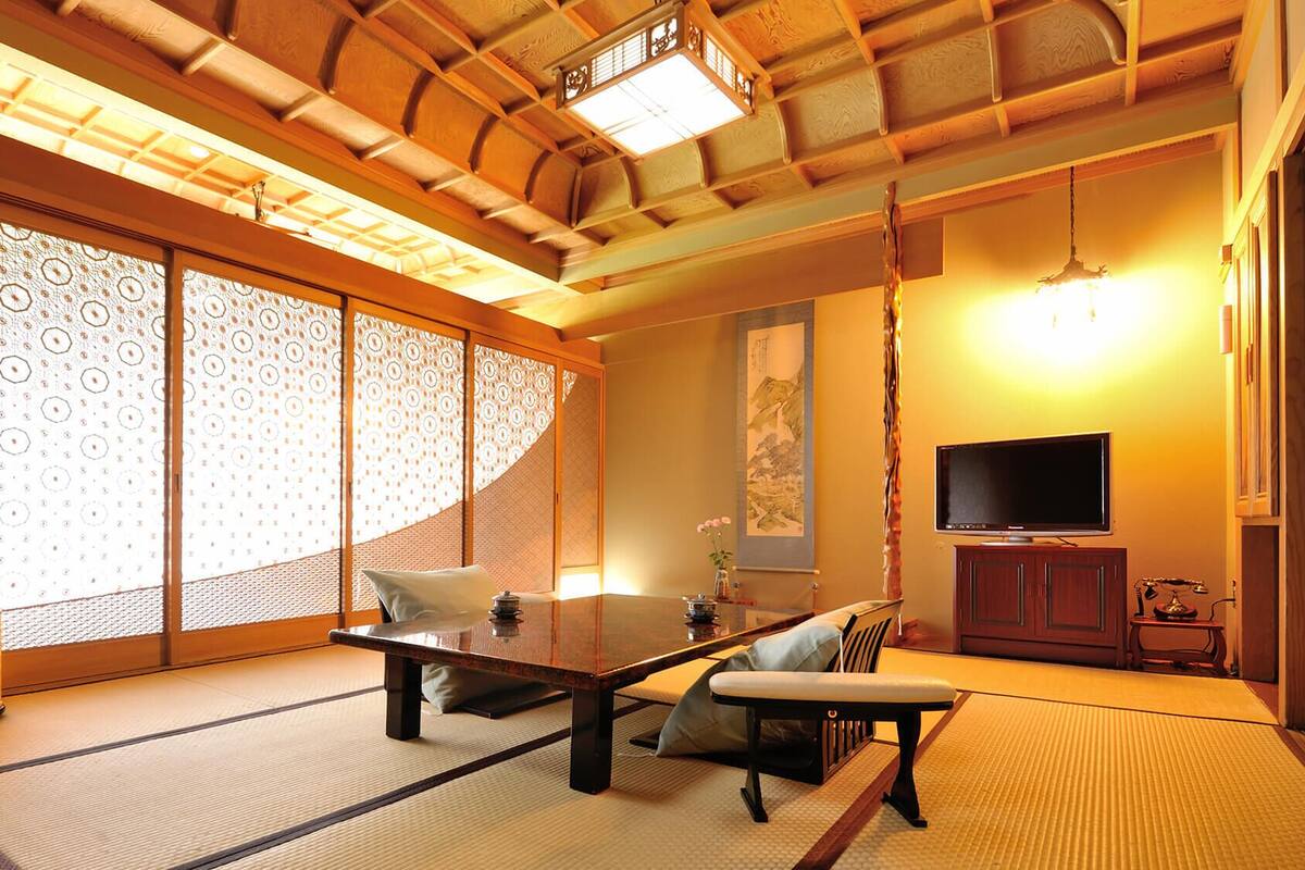 A traditional Japanese room with tatami flooring, a low table, a sofa, a TV, and sliding doors with patterned glass.