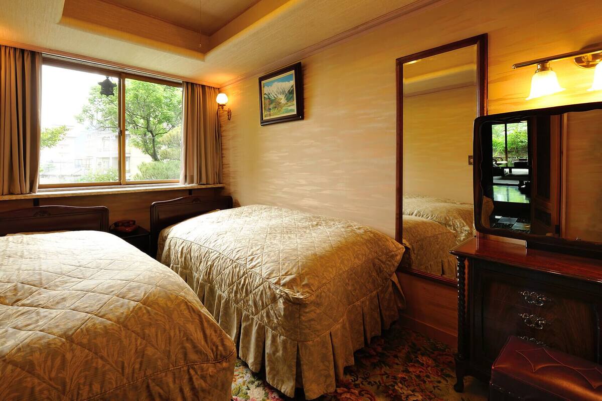 A hotel room with two beds, a large window, a mirror, and a wooden dresser.
