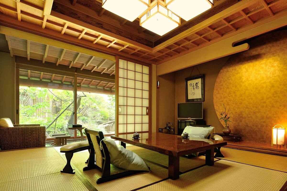 A traditional Japanese room with tatami flooring, a low table, cushions, a sliding door, and a large round wall feature.