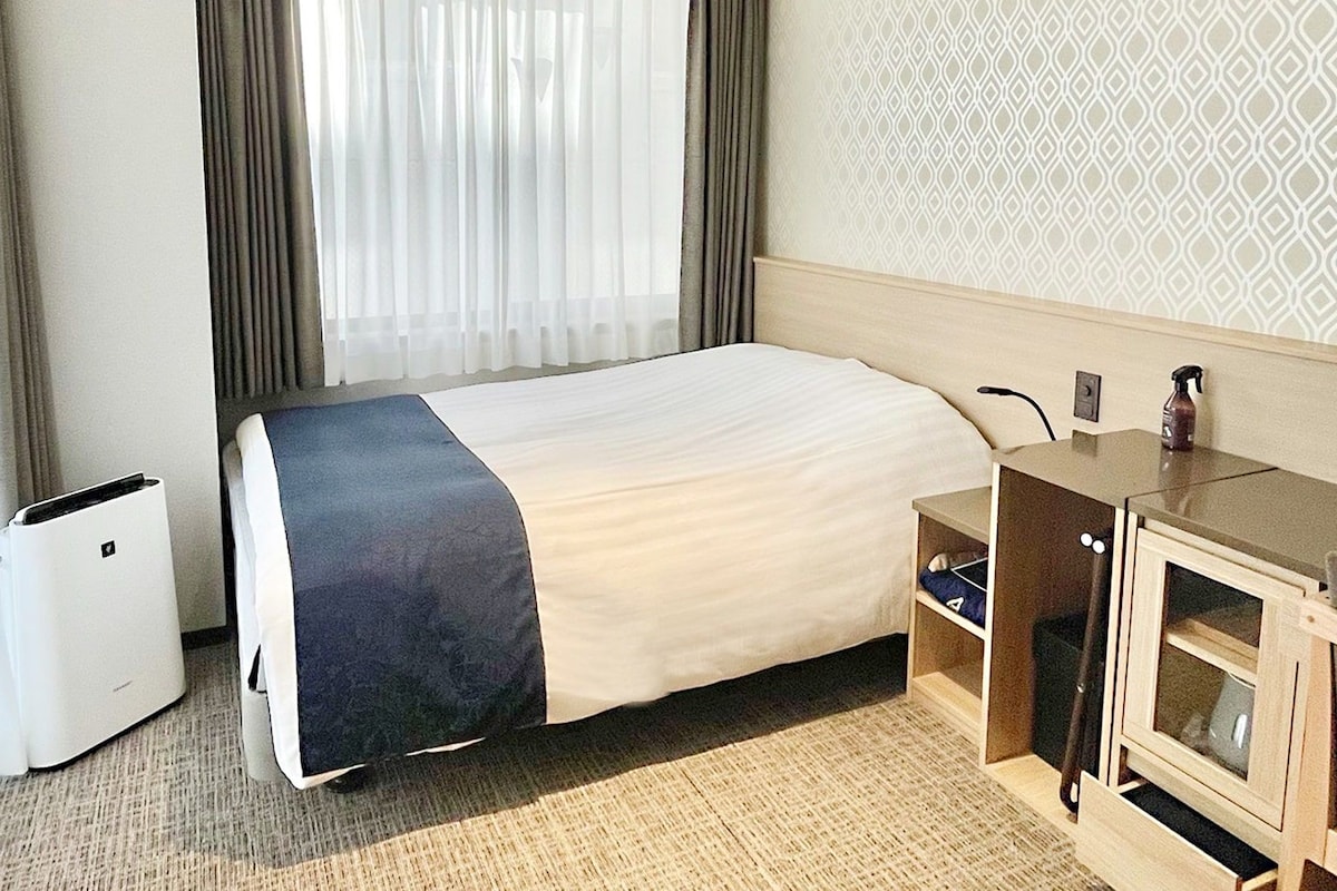 Hotellihuone, jossa on sänky, työpöytä, tuoli, pieni kaappi ja roskakori.