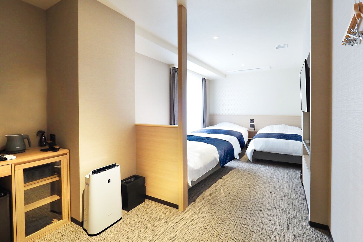 Une chambre d’hôtel équipée d’un bureau, d’un petit réfrigérateur, d’un lit avec une tête de lit et d’une fenêtre avec des rideaux.
