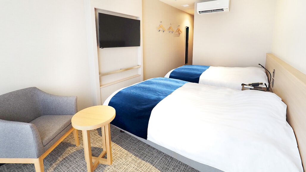 Quarto de hotel com duas camas, televisão, mesa pequena e sofá.