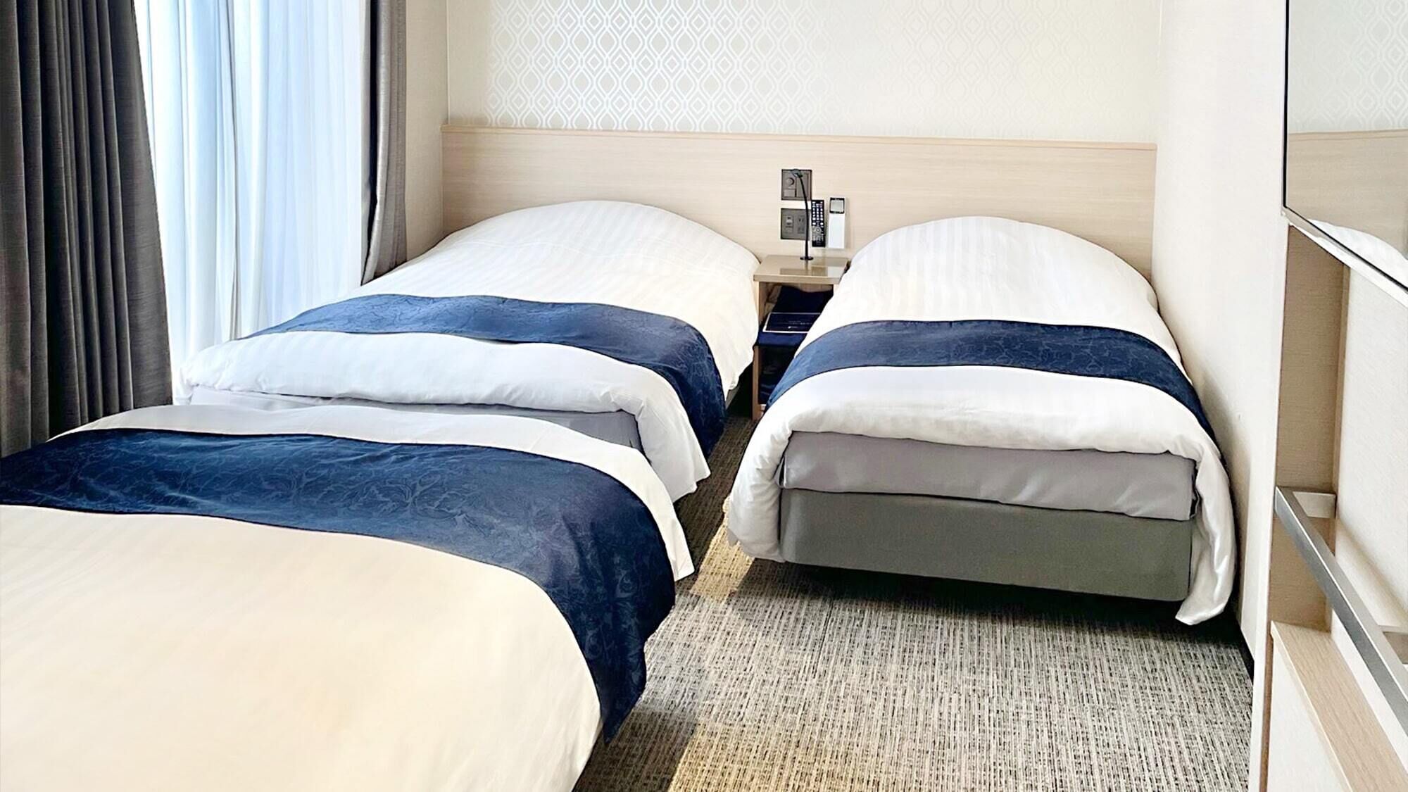 Habitación de hotel con dos camas, una mesita de noche con teléfono y lámpara, y un papel tapiz estampado.