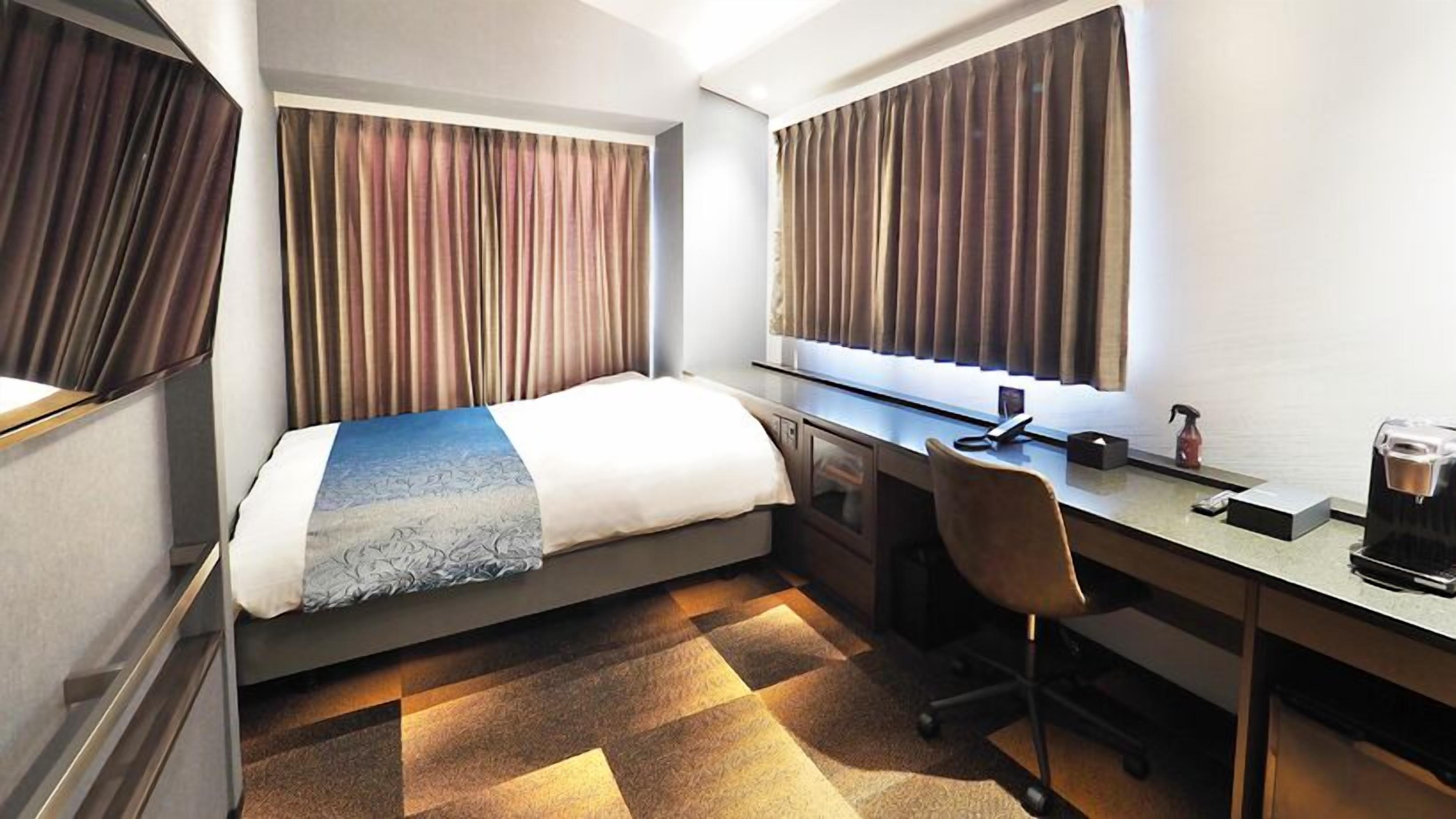 Quarto de hotel com cama, escrivaninha, cadeira e cortinas.