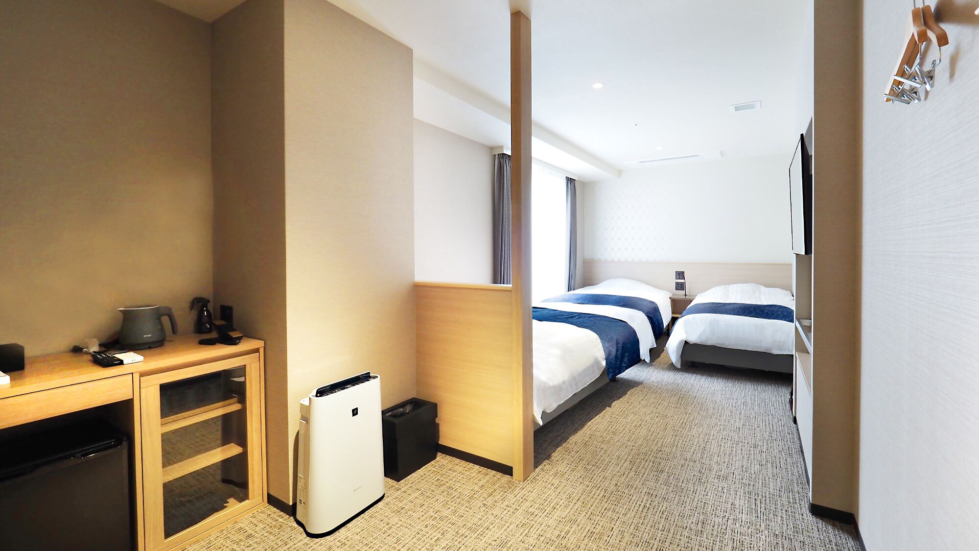 Habitación de hotel con escritorio, refrigerador pequeño, cama con cabecera y ventana con cortinas.