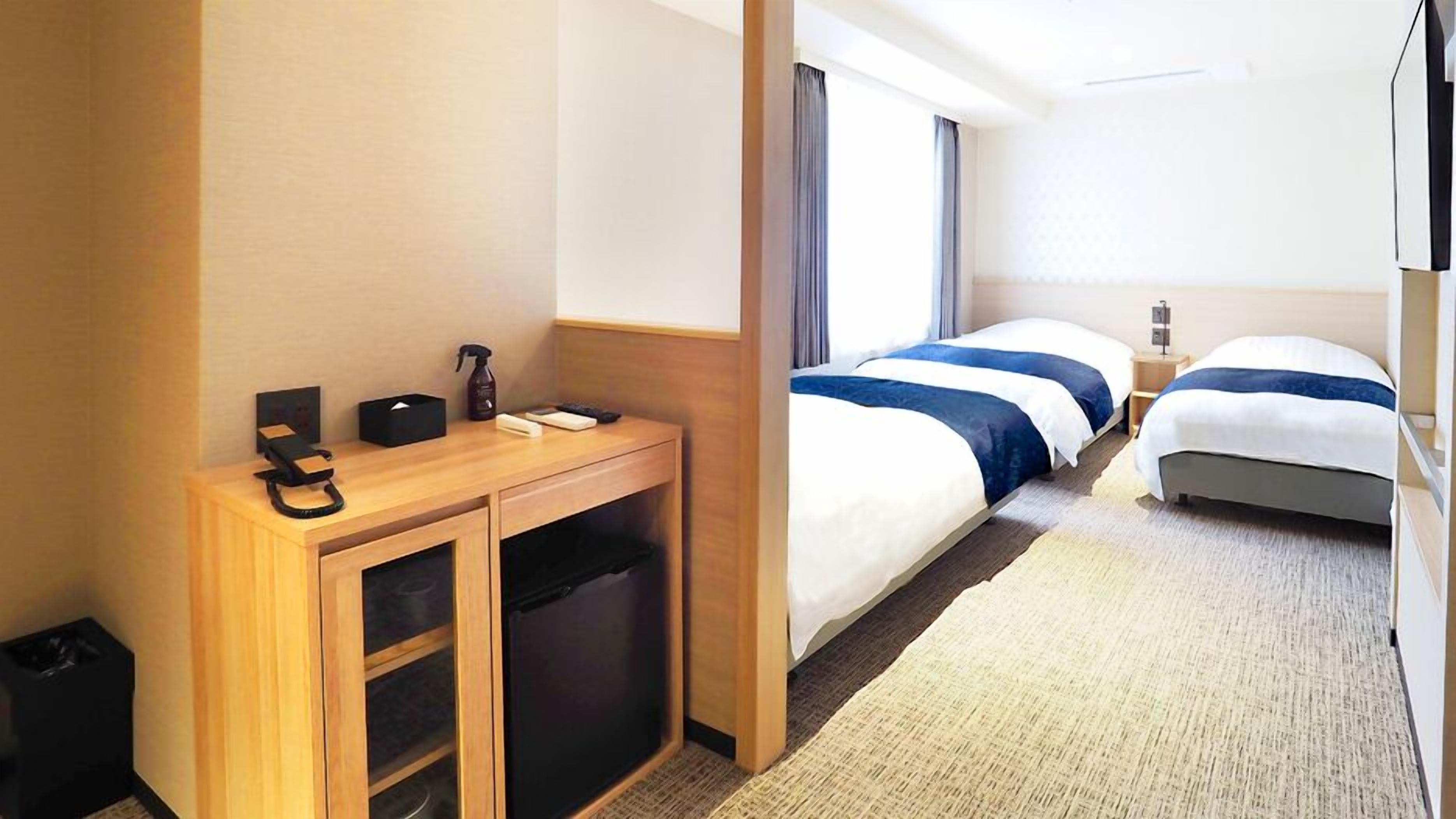 Quarto de hotel com secretária de madeira, duas camas, televisão e janela com cortinas.