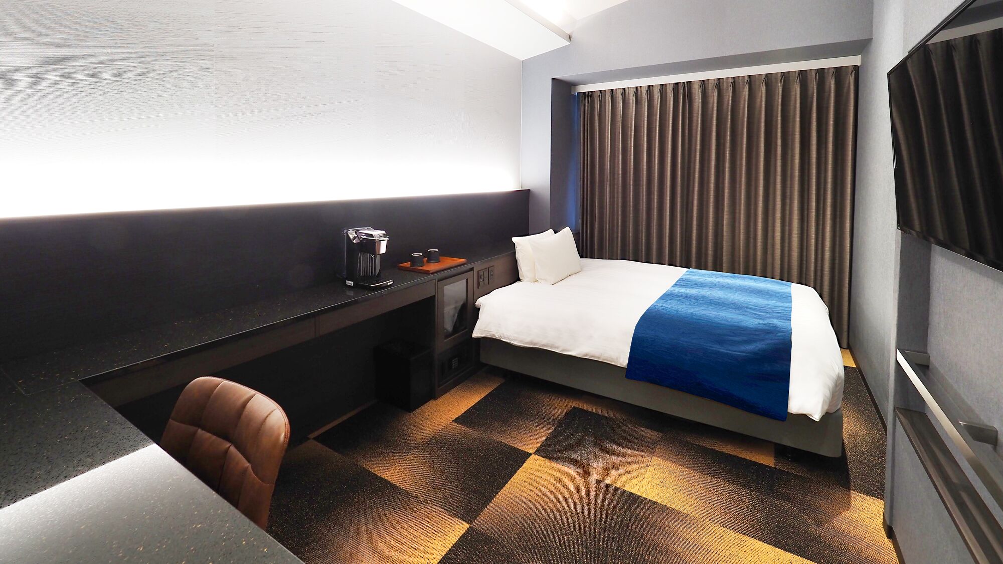 Habitación de hotel con cama, escritorio, silla, cafetera y ventana con cortinas.