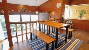 A wooden interior with a dining area featuring a wooden table and benches, a striped rug, and a view of the outdoors through large windows. - Greenmist Atami Shizenkyo (Atami)