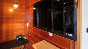 A room with wooden panel walls, a large black TV, a wooden bench, and a hanging light fixture. - Greenmist Atami Shizenkyo (Atami)