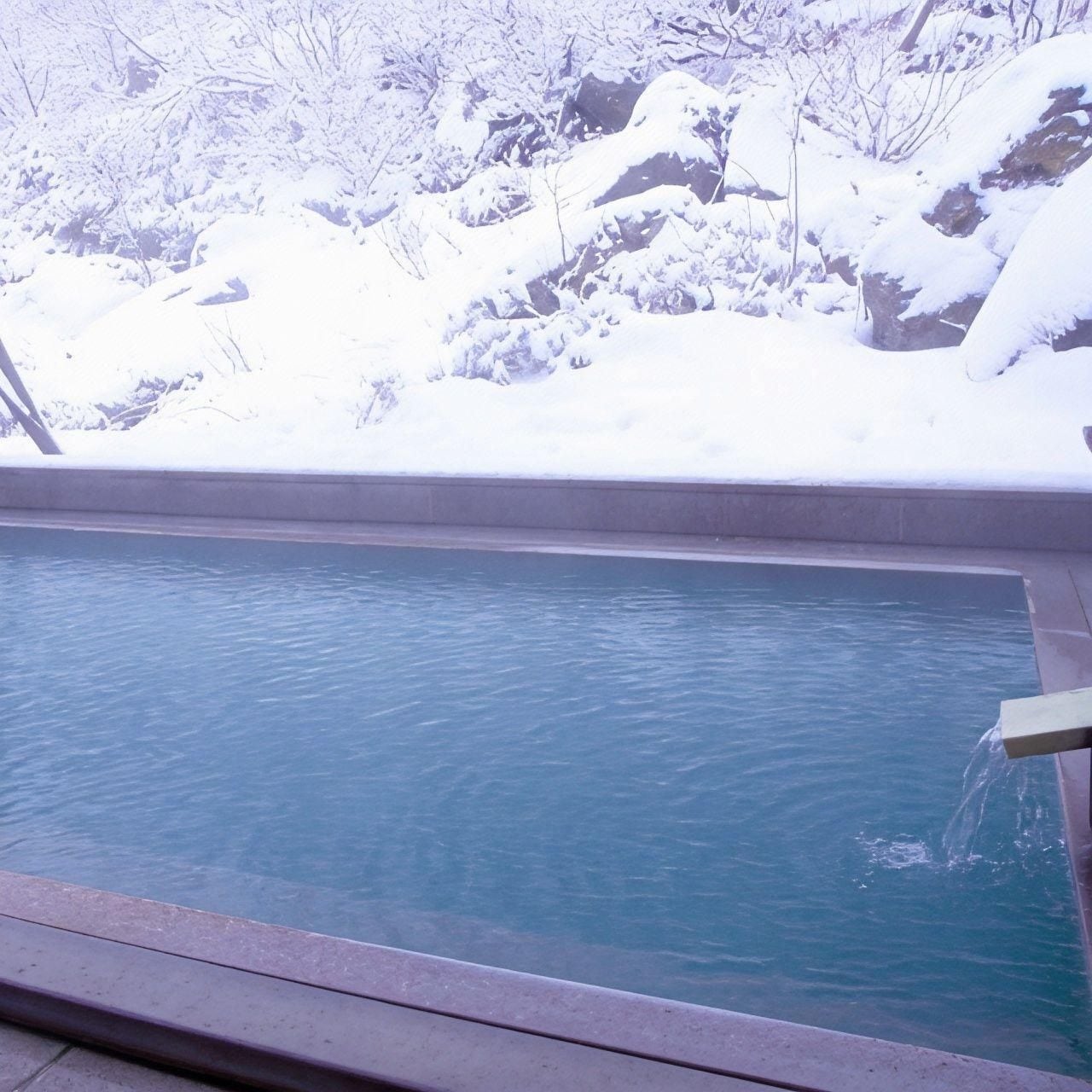 A rectangular pool with clear blue water, surrounded by snow-covered rocks and trees.