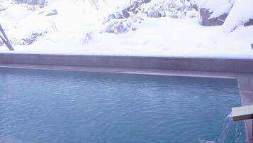 A rectangular pool with clear blue water, surrounded by snow-covered rocks and trees.