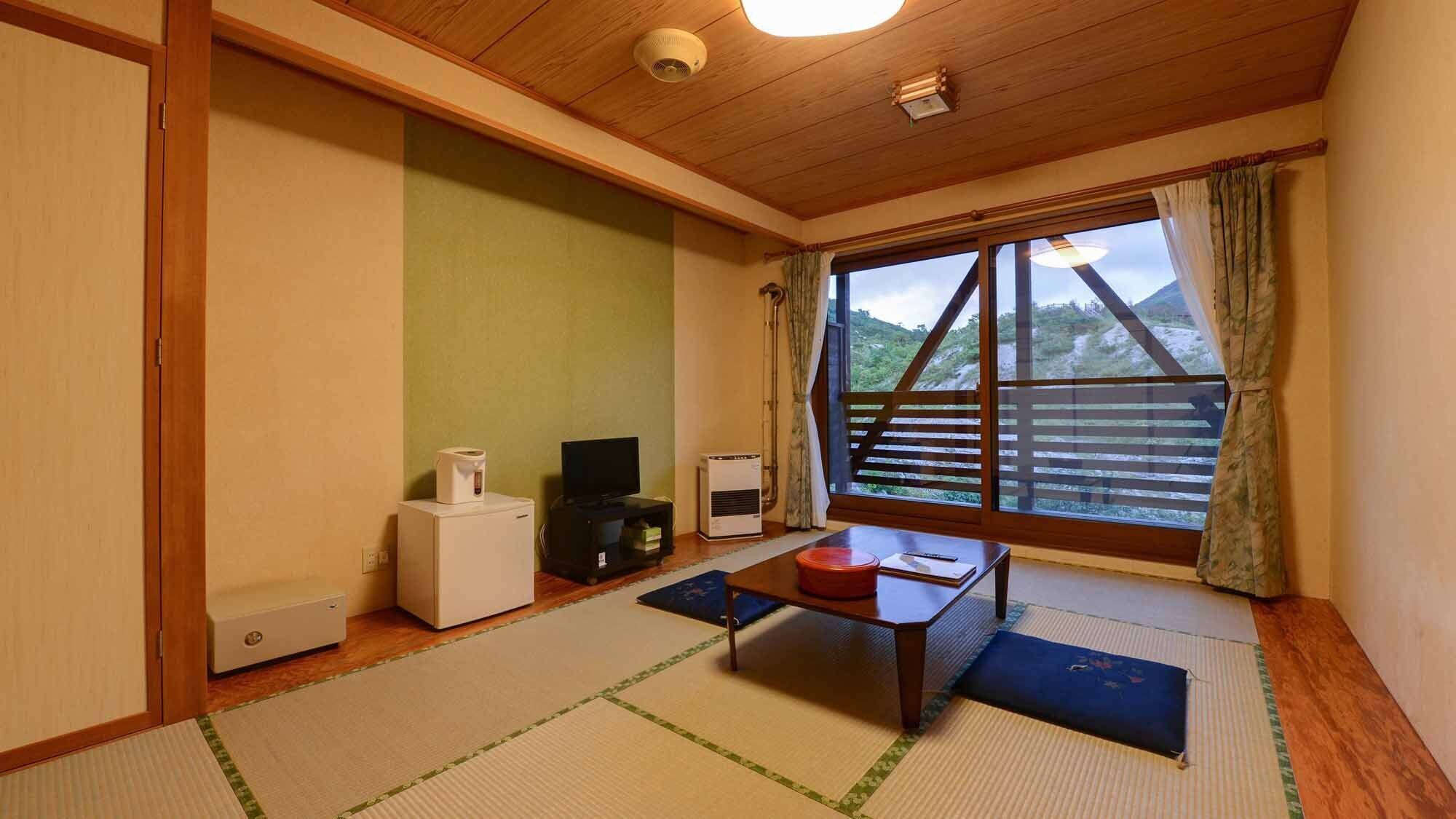 A room with tatami flooring, a television, a heater, and a window with a view of a wooden structure.