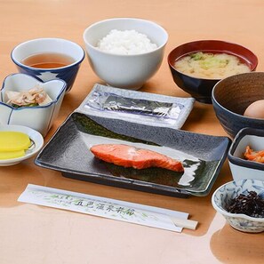 Une table où l’on peut voir différents plats japonais, notamment du riz, de la soupe et du poisson, présentés sur une assiette.