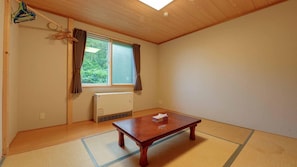 Une pièce avec un sol recouvert de tatamis, une table en bois, un radiateur et une fenêtre avec des rideaux.