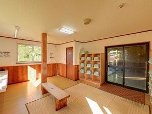 Une pièce avec un plancher en bois, un banc, un meuble en bois contenant des récipients verts et une porte coulissante en verre.