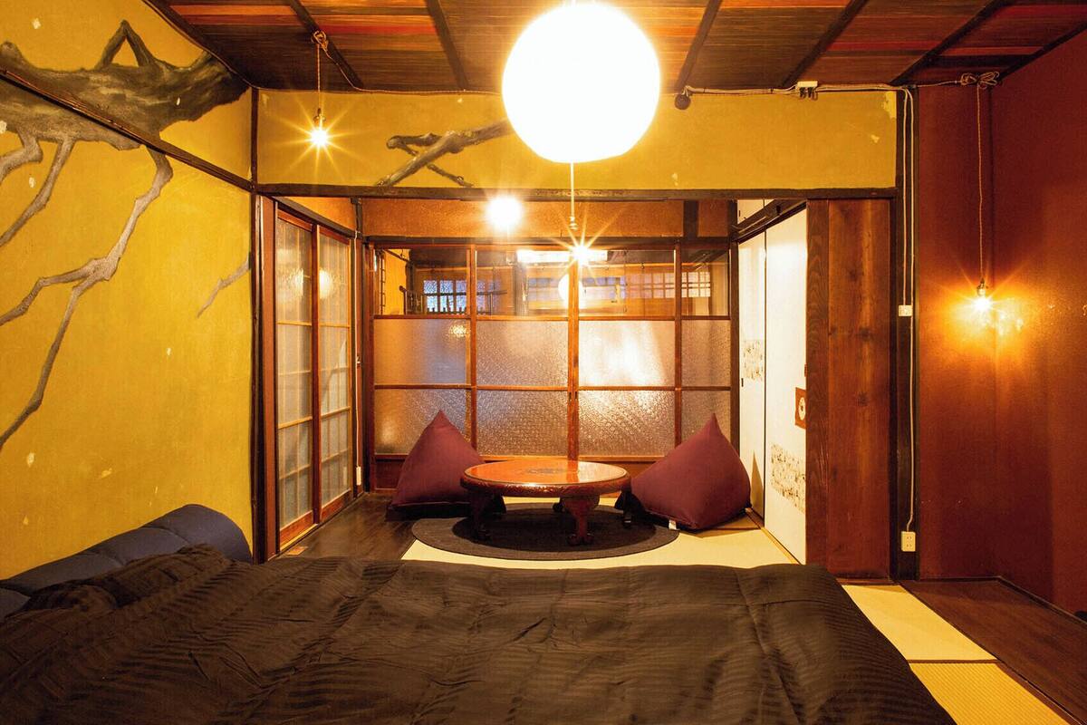 Una habitación japonesa tradicional con suelo de tatami, una mesa baja con cojines, puertas correderas y una lámpara colgante.