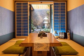 Et traditionelt japansk rum med tatamimåtter, et lavt bord med en vase og udsigt til en have gennem shoji-skærme.