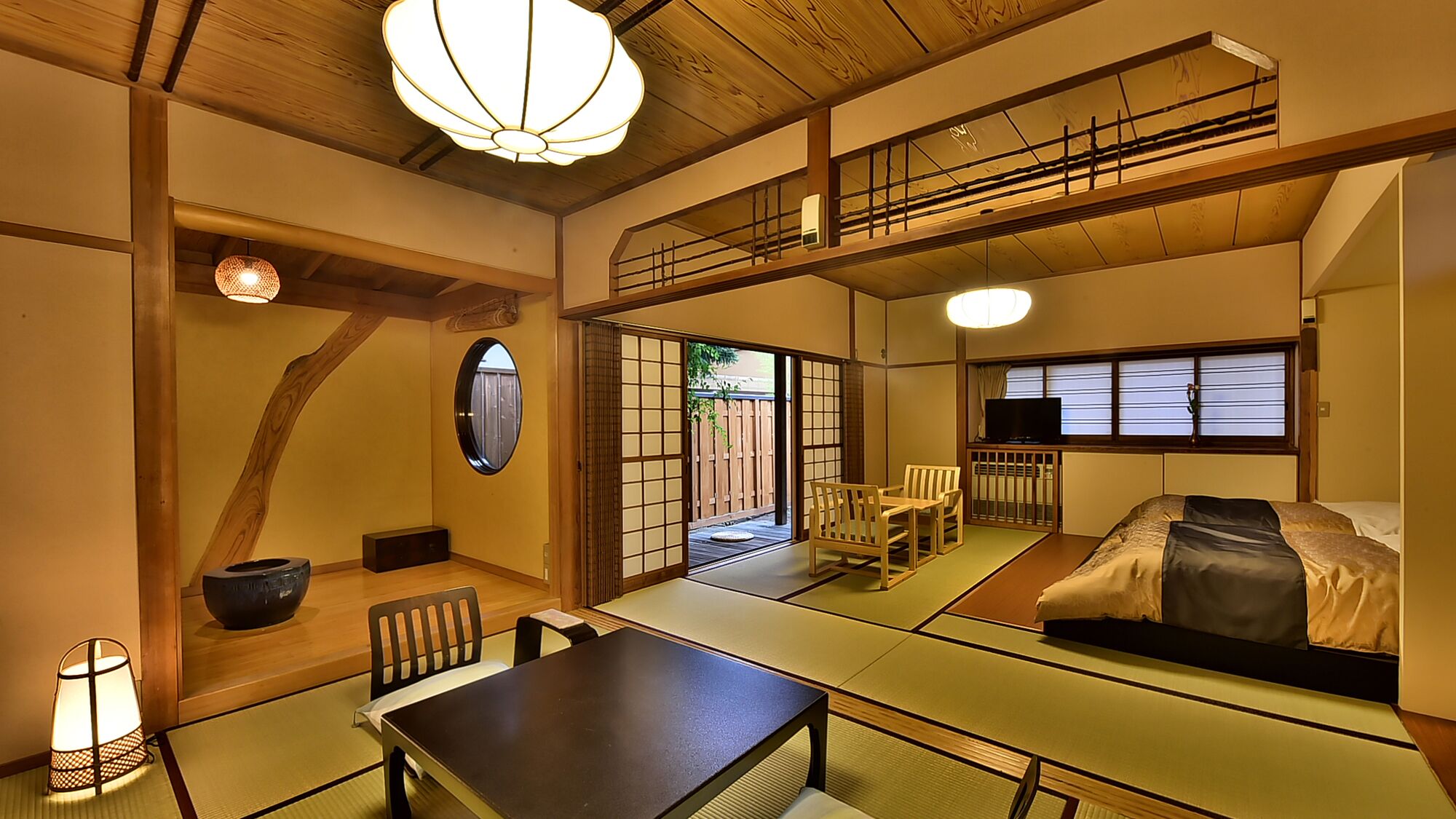 A traditional Japanese-style room with tatami flooring, a low table, chairs, a bed, and a television.