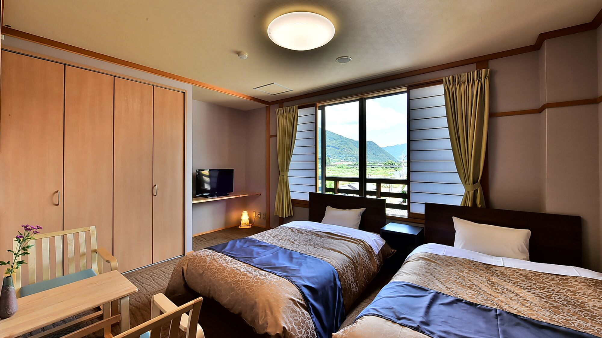 A hotel room with two beds, a TV, a desk, and a window with curtains.