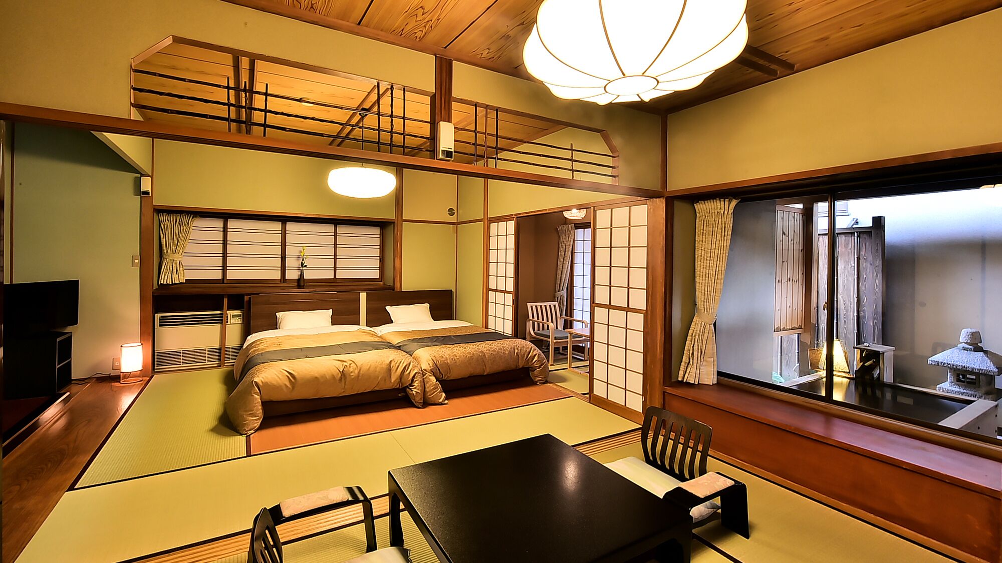 A traditional Japanese-style room with tatami flooring, a bed with a wooden headboard, a television, and a view through a shoji screen.