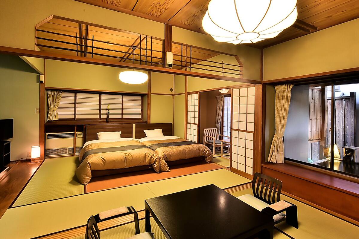 A traditional Japanese-style room with tatami flooring, a bed with a wooden headboard, a television, and a view through a shoji screen.