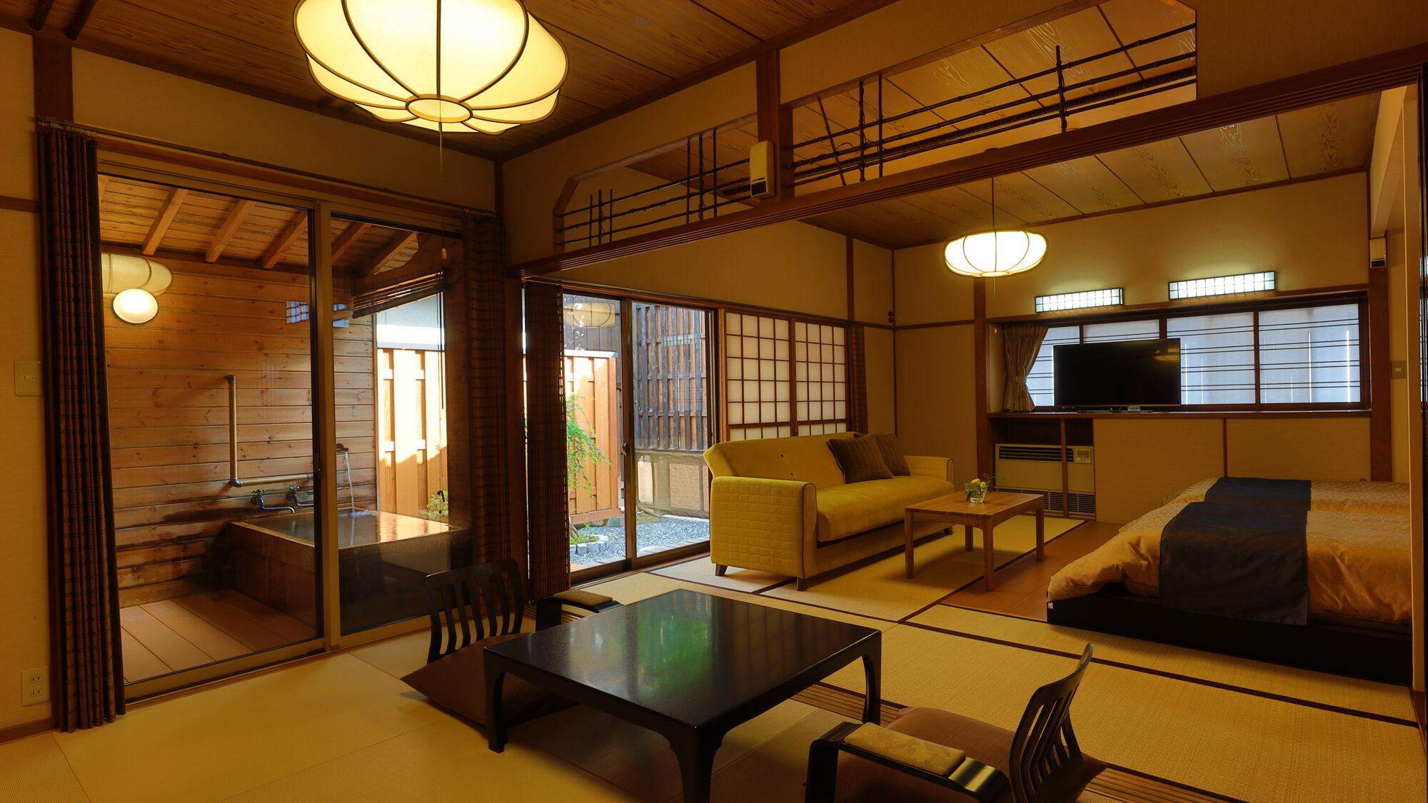 A traditional Japanese-style room with tatami flooring, a sofa, a table, and a television.