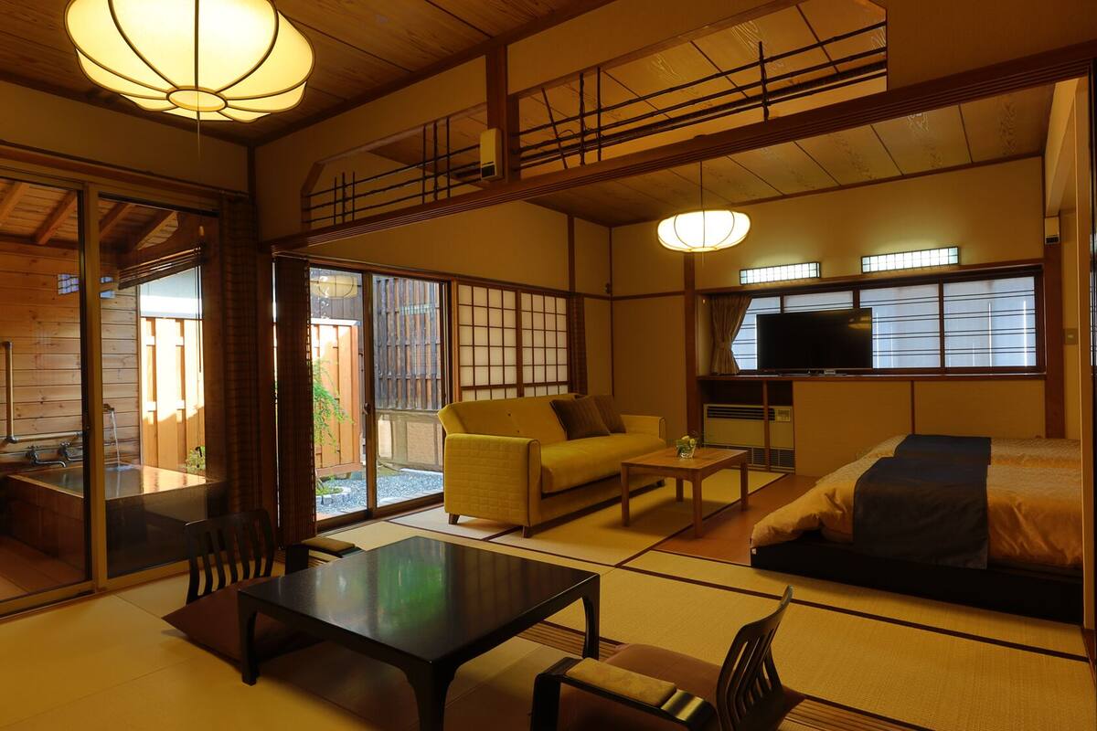 A traditional Japanese-style room with tatami flooring, a sofa, a table, and a television.