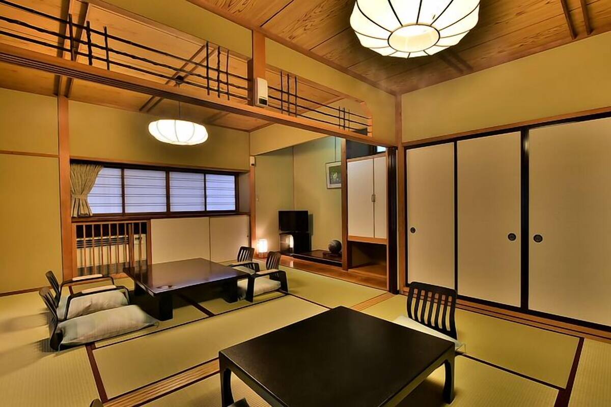 A traditional Japanese room with tatami flooring, a low table, a sofa, sliding doors, and a ceiling light fixture.