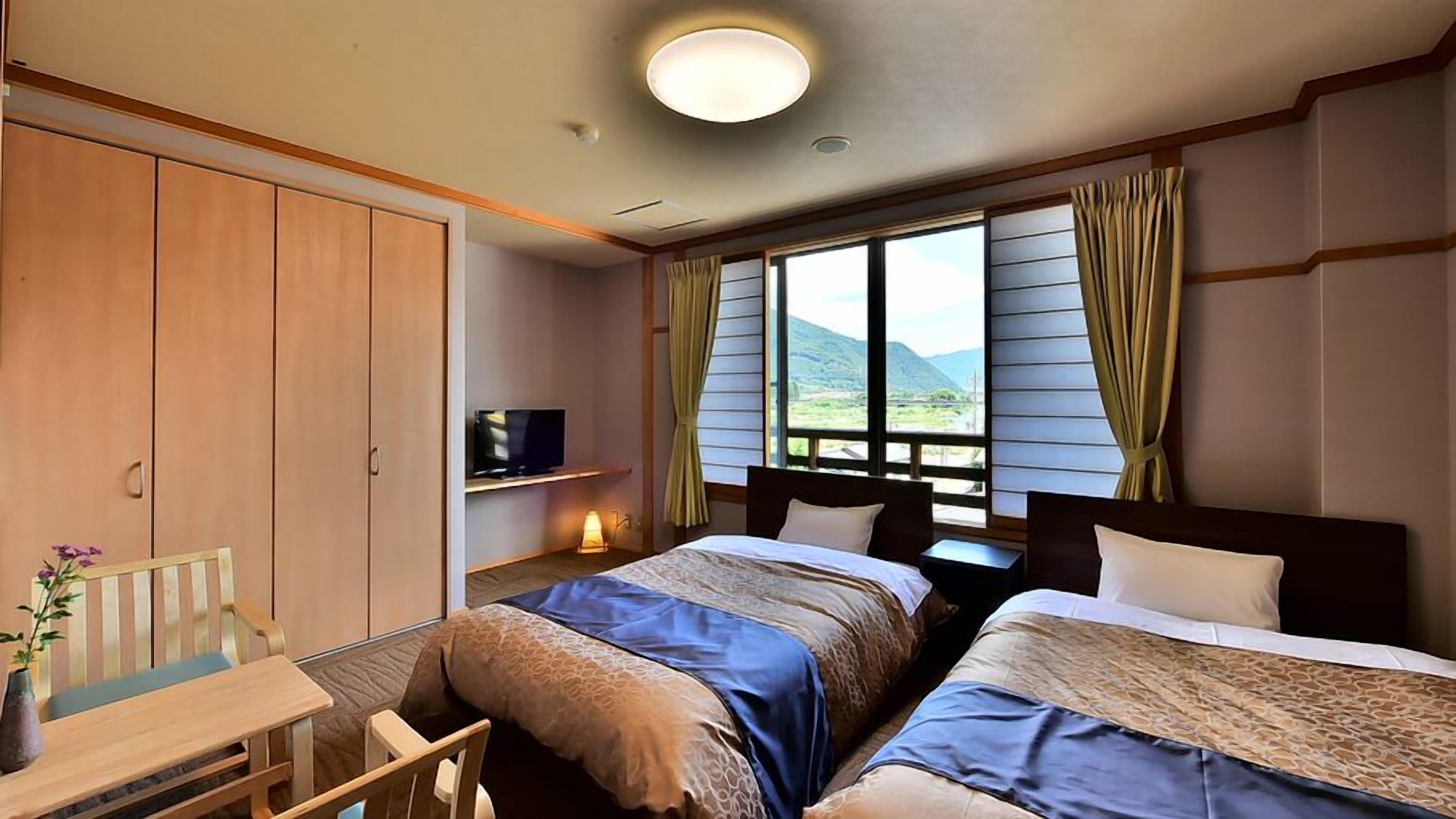 A hotel room with two beds, a desk, a TV, and a window with curtains.