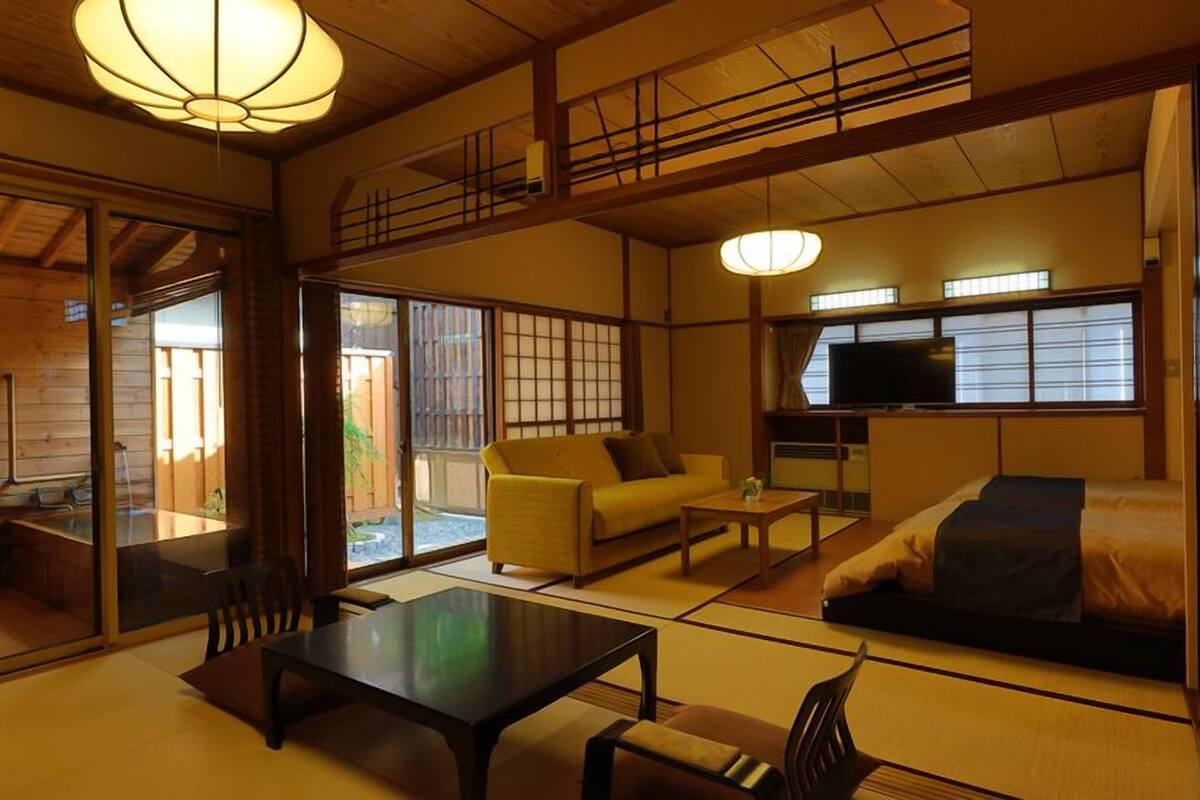 A traditional Japanese-style room with tatami flooring, a low table, a sofa, and a television.