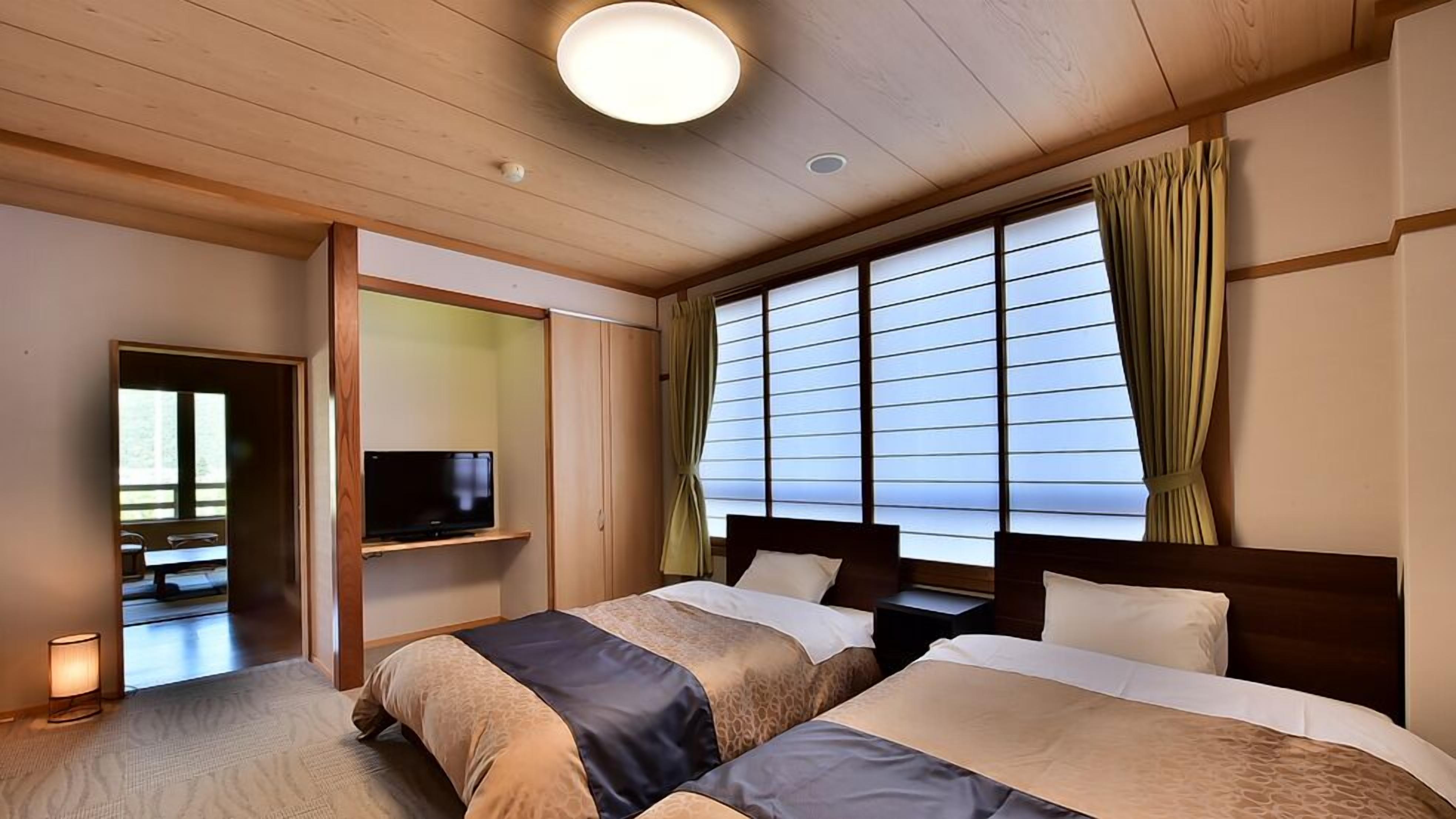 A hotel room with two beds, a television on a shelf, a window with curtains, and a ceiling light.