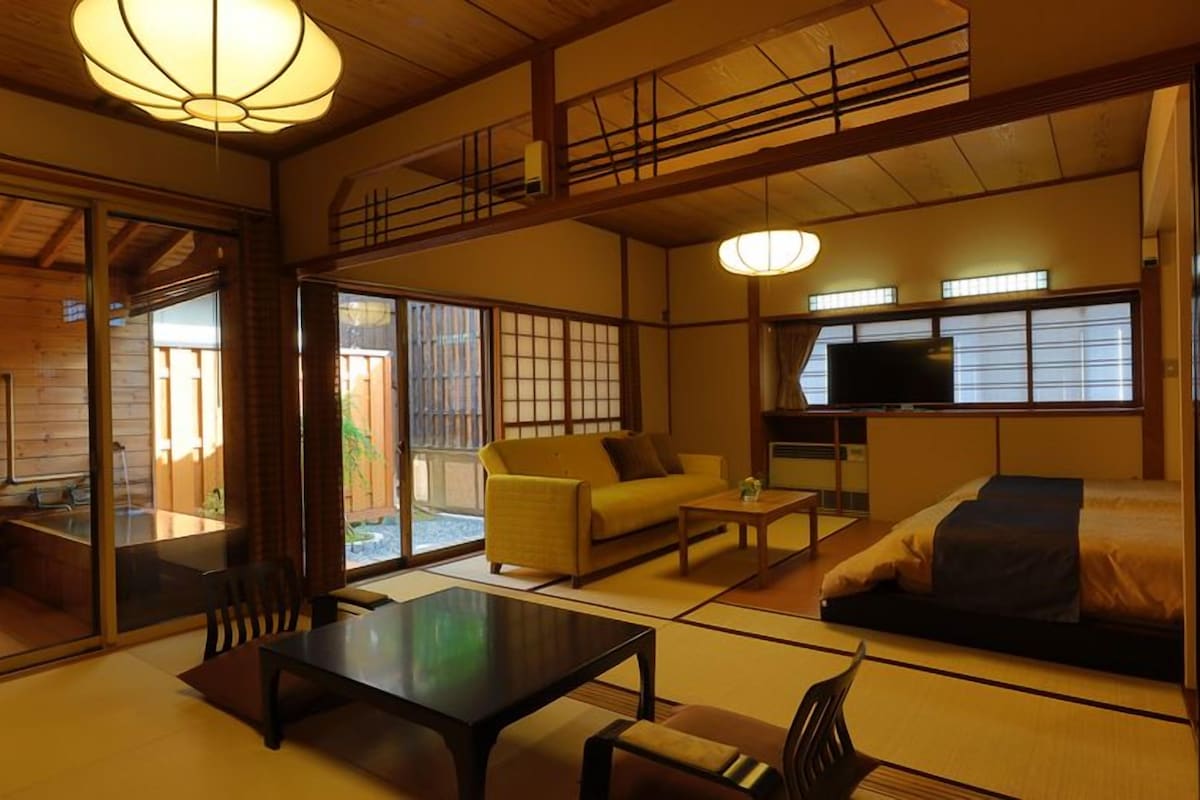 A traditional Japanese-style room with tatami flooring, a low table, a sofa, and a television.