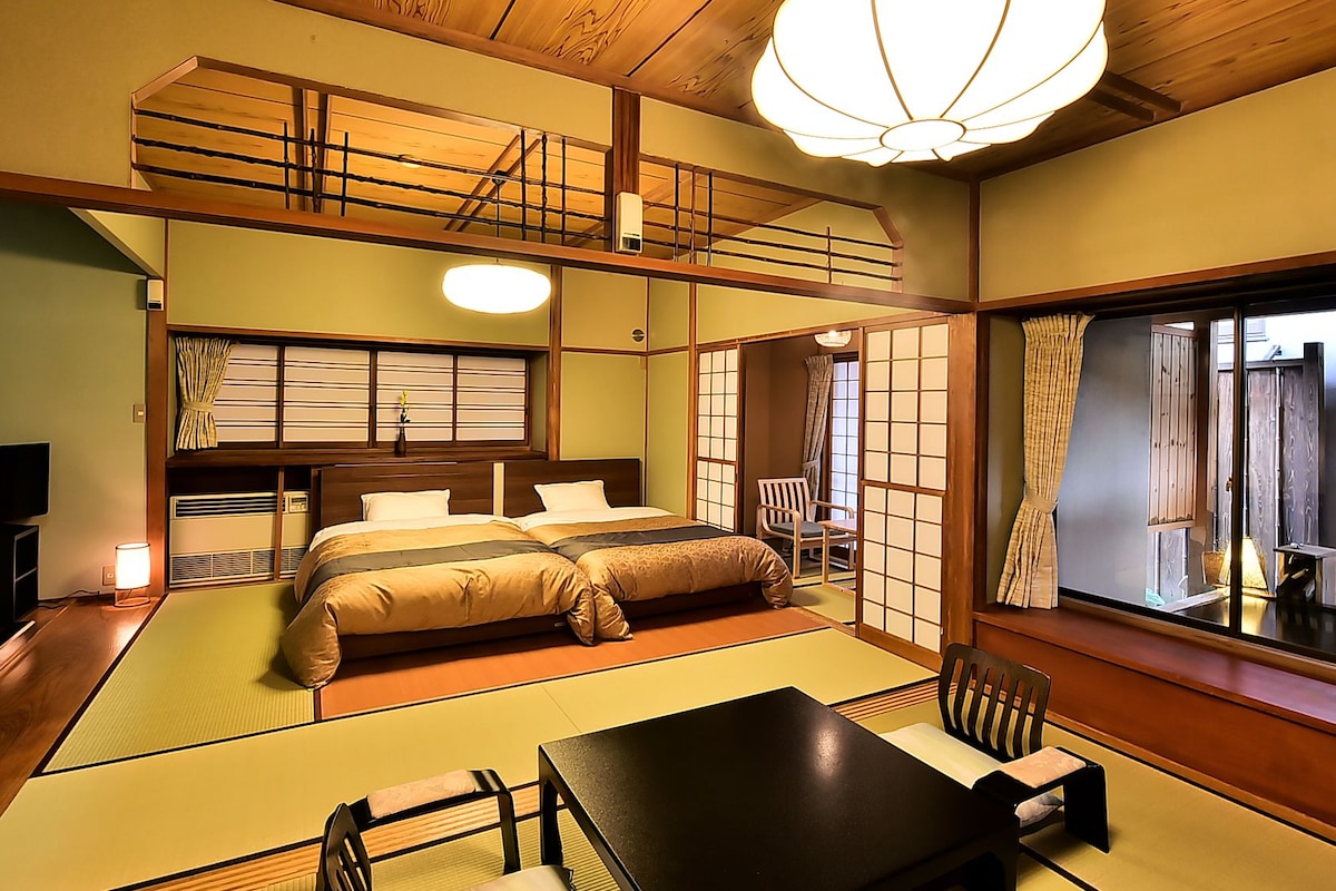A traditional Japanese-style room with tatami flooring, a bed with a wooden headboard, a television, and a view through a shoji screen.