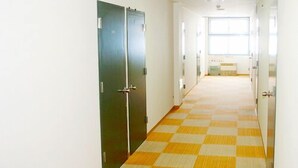 Un couloir avec un tapis à carreaux, des portes vertes et une fenêtre au fond.