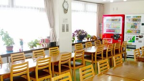 Un espace repas avec des tables et des chaises en bois, une horloge au mur et des distributeurs automatiques.