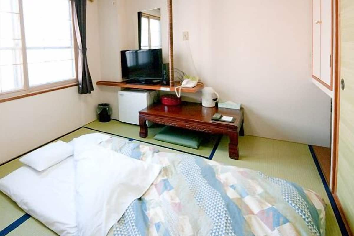 A traditional Japanese room with tatami flooring, a low wooden desk, a television, and a futon bed.
