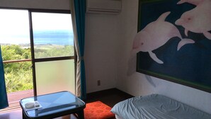 A room with a glass table, a sofa, a painting of dolphins, and a view of the ocean. - K2 Cottage (Hachijo)